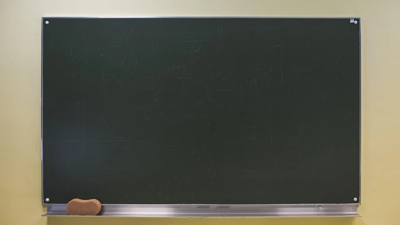 Un tableau noir vide dans son cadre, la brosse posée sur la rainure